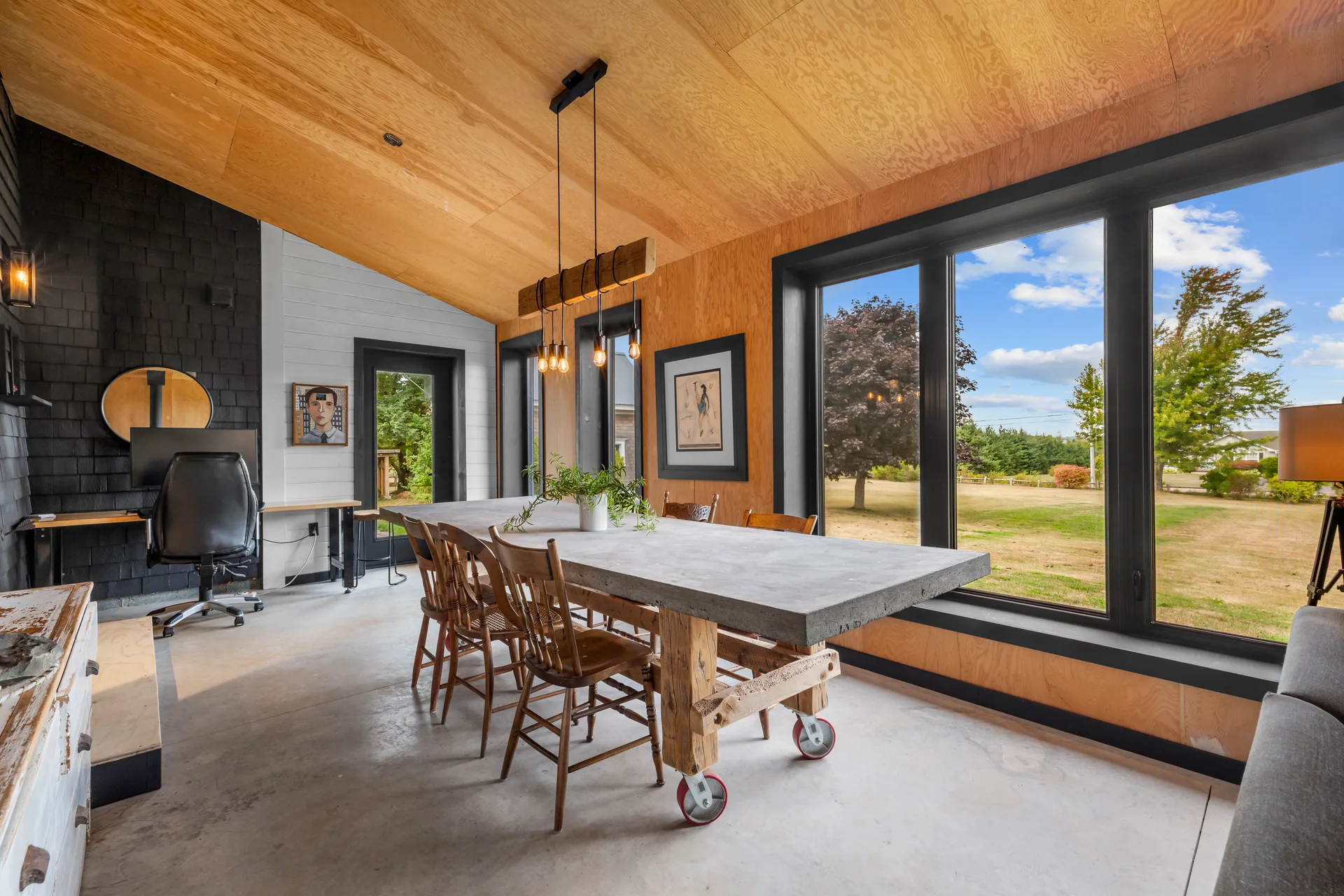 Sun-filled dining area in the addition with concrete floors, plywood ceiling, and black-framed windows