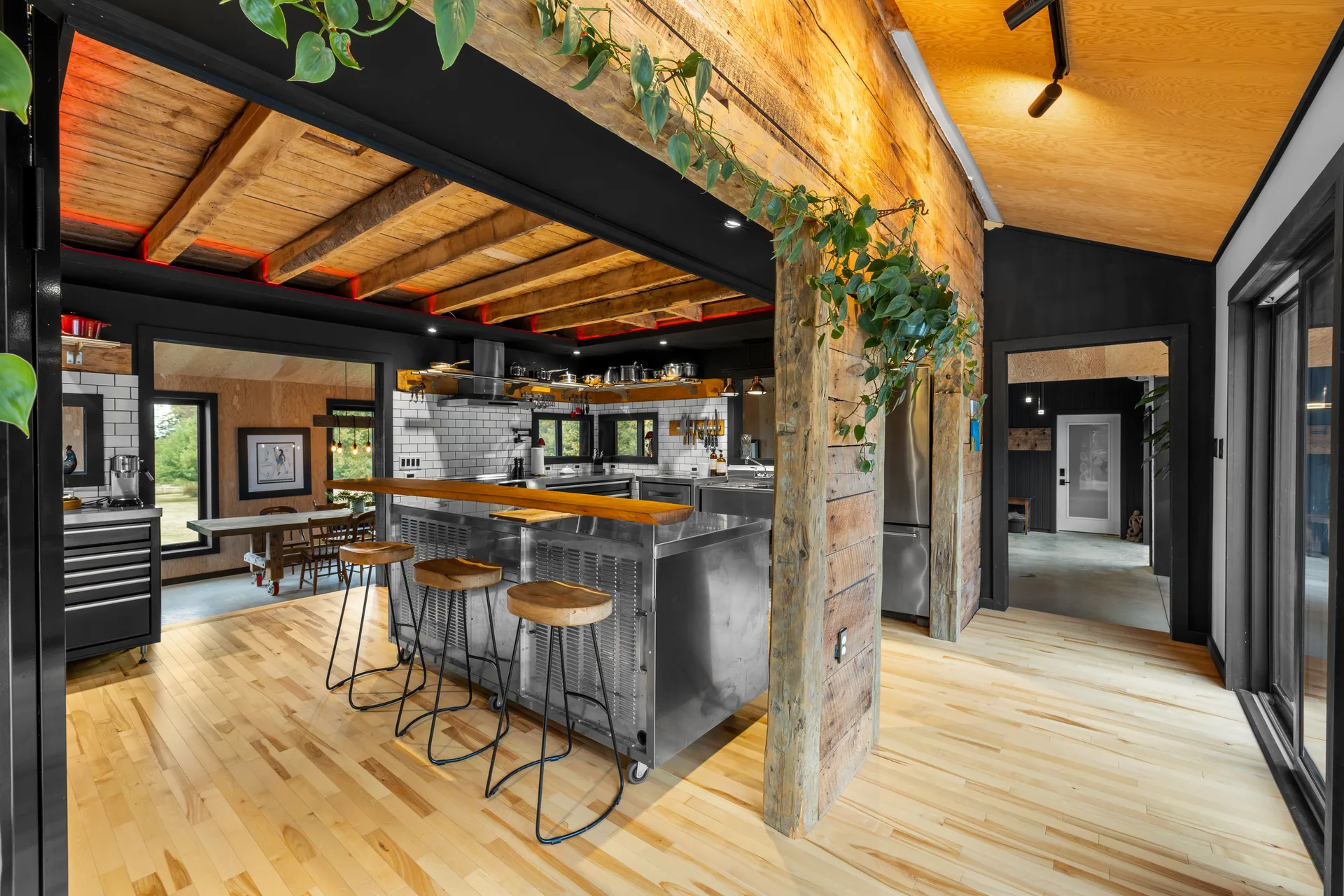 Wide-angle chef's kitchen with stainless steel island on wheels, exposed wood beams, reclaimed wood pillars, and black cabinetry