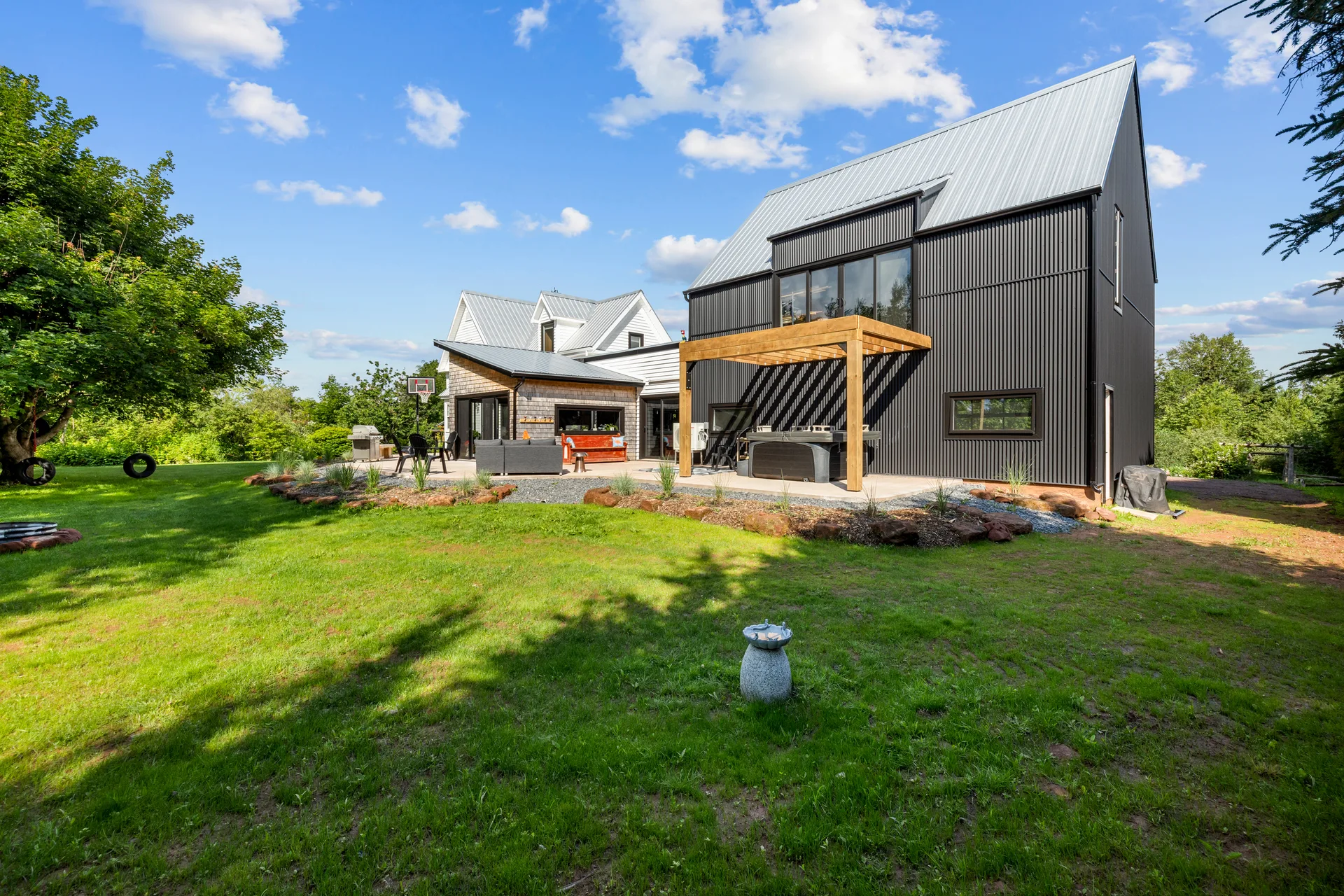 Backyard view of the modern barn-inspired addition with dark metal siding, large wood pergola, and standing seam metal roof