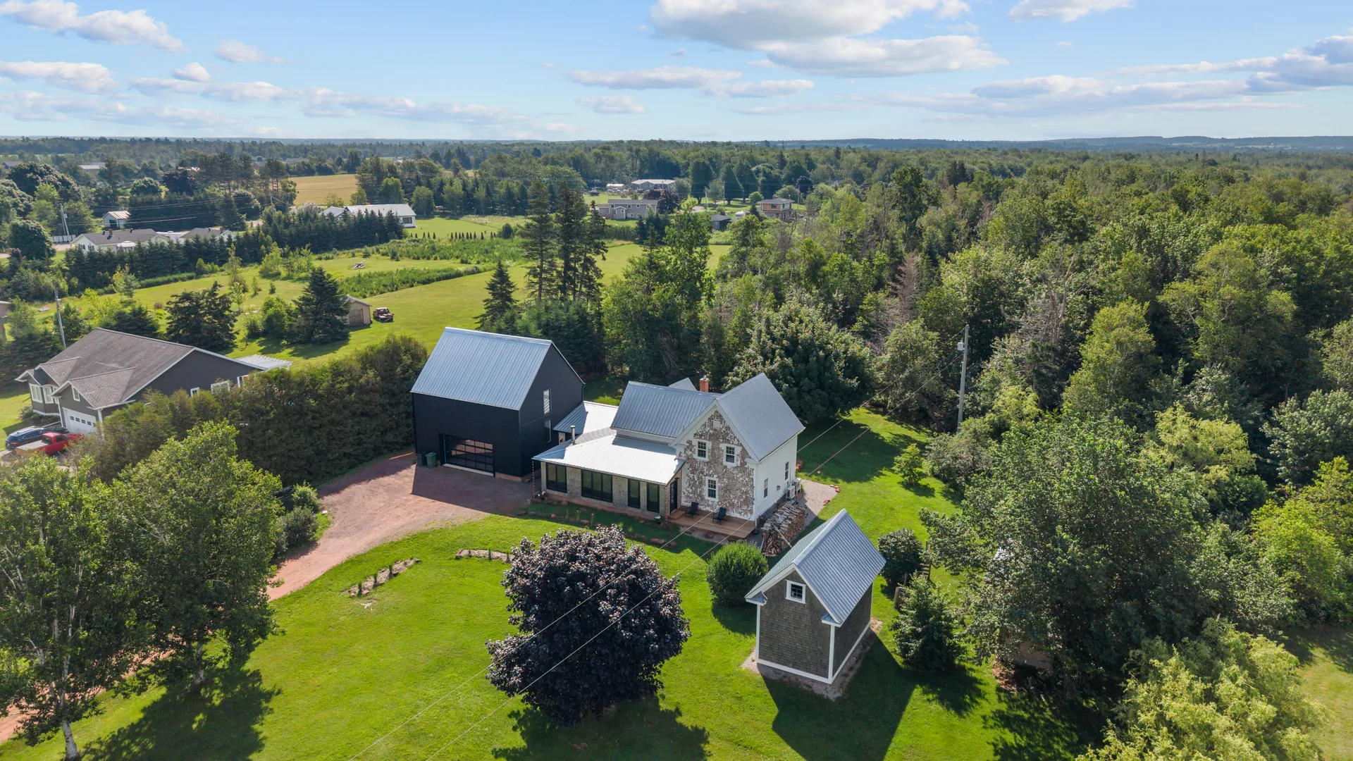 Aerial view of the farmhouse, oversized garage, and surrounding homestead with mature trees and green lawns