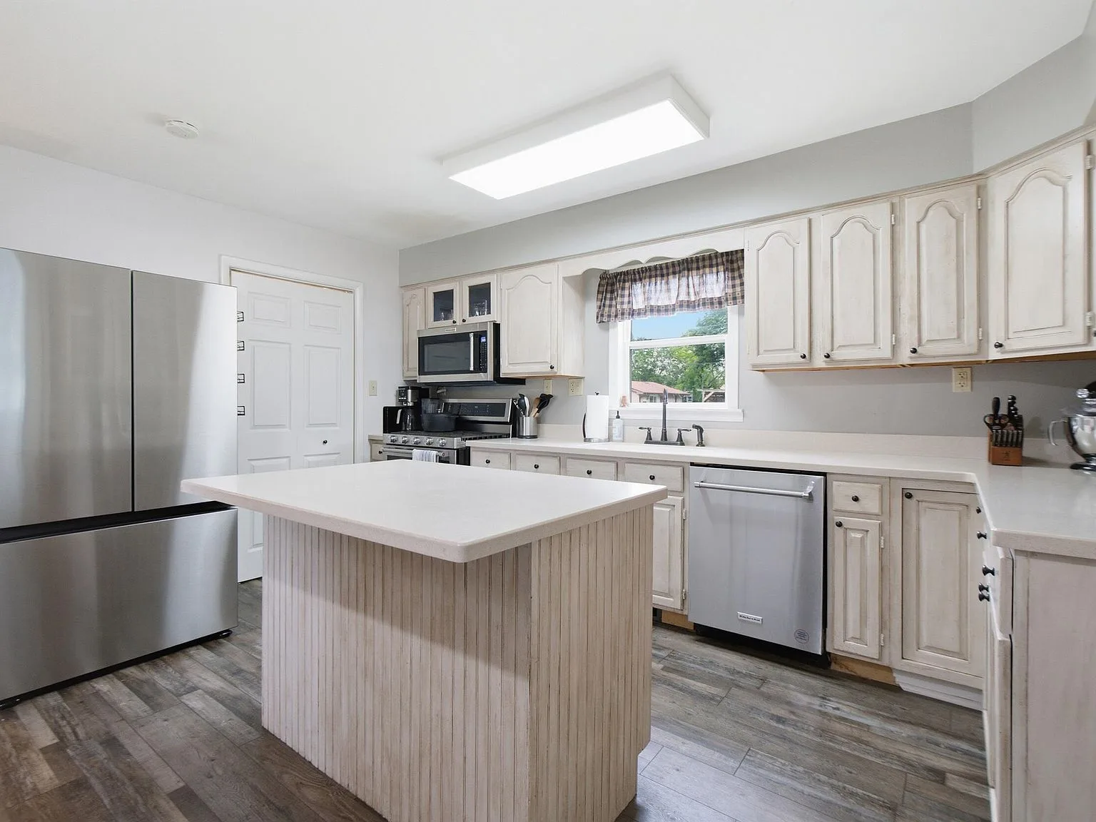 Wide-angle kitchen view with off-white cabinetry and wood-look flooring