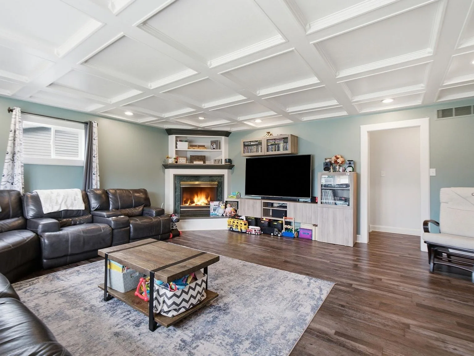 Living room with coffered ceiling, gas fireplace, and wood-look flooring