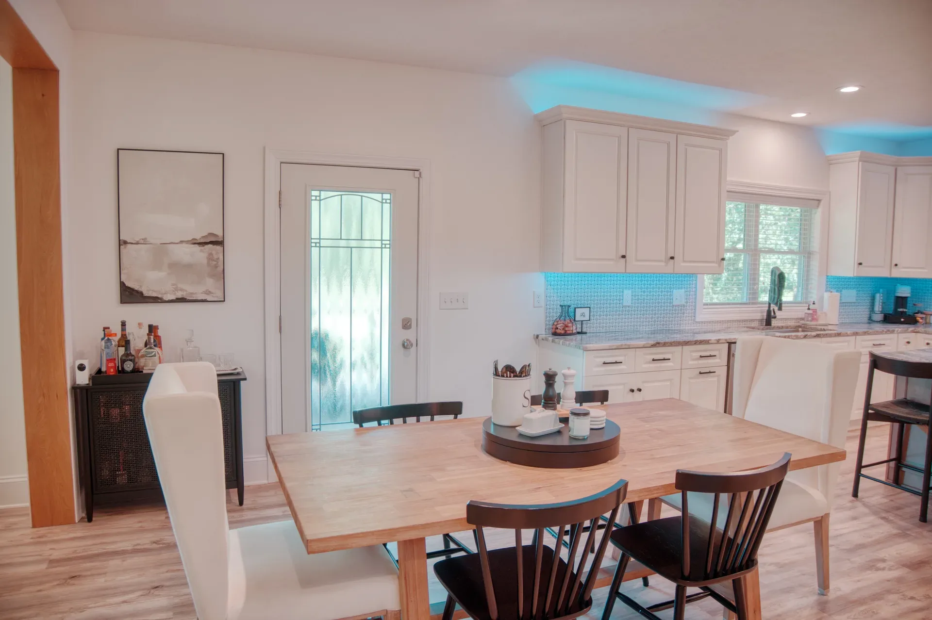 Kitchen and dining area with white cabinetry, blue under-cabinet lighting, and wood dining table