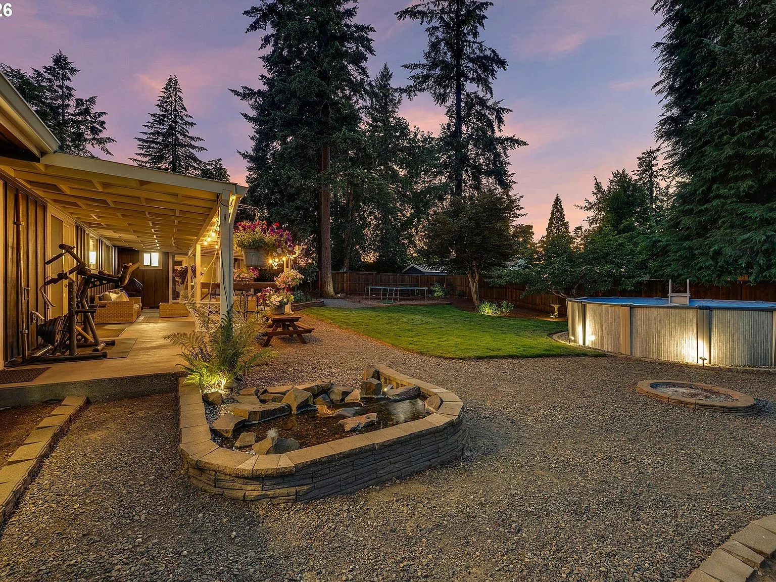 Backyard at dusk with covered patio, pool, and stone water feature