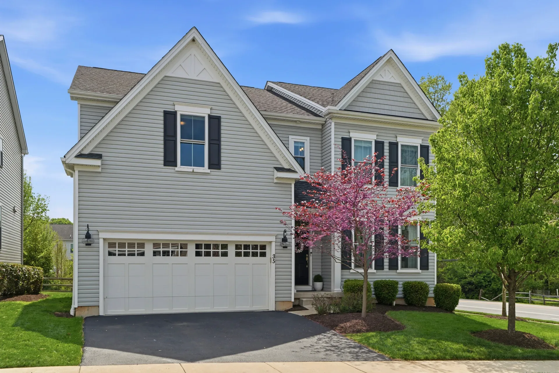 Front facade of 35 Dickinson Lane, a colonial home with grey siding, dark shutters, and flowering trees