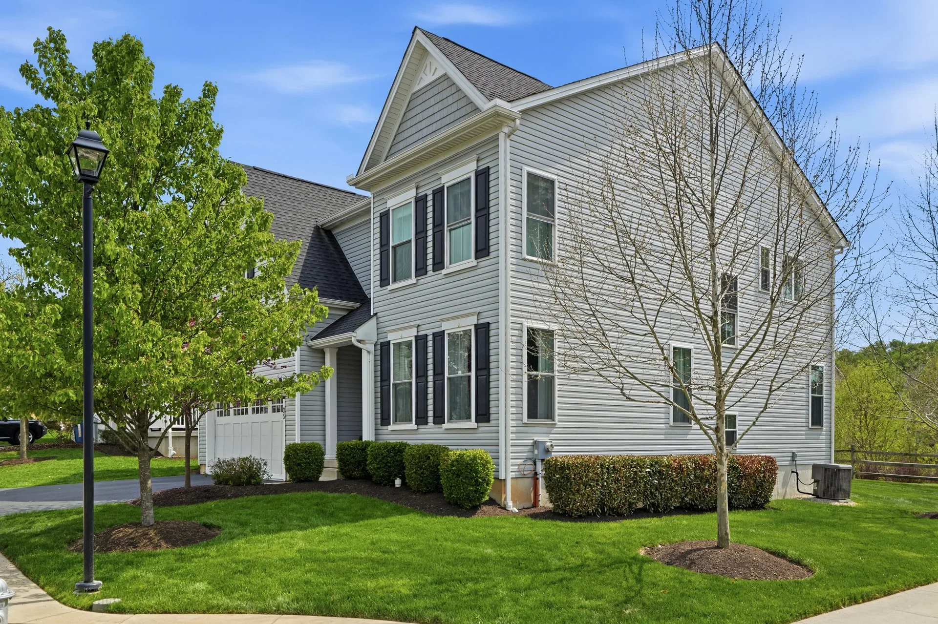 Side profile view of the home with grey siding, dark shutters, and manicured bushes