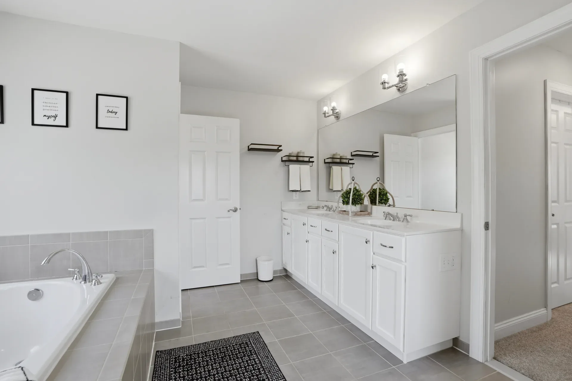 Master bathroom with dual vanity, soaking tub, and grey tile surround