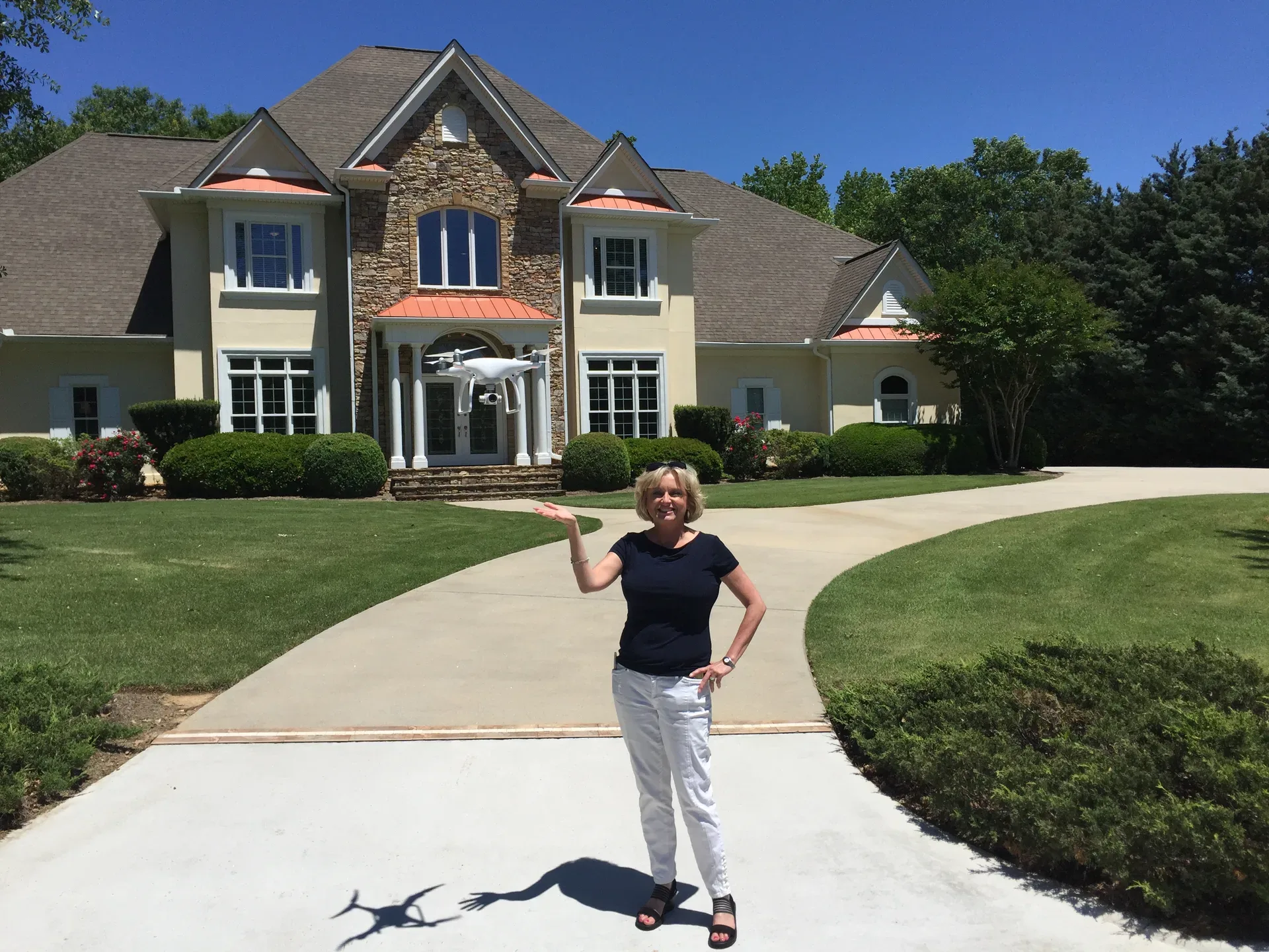 Lisa Harris standing in front of a home holding a camera drone, demonstrating hands-on modern real estate marketing technology