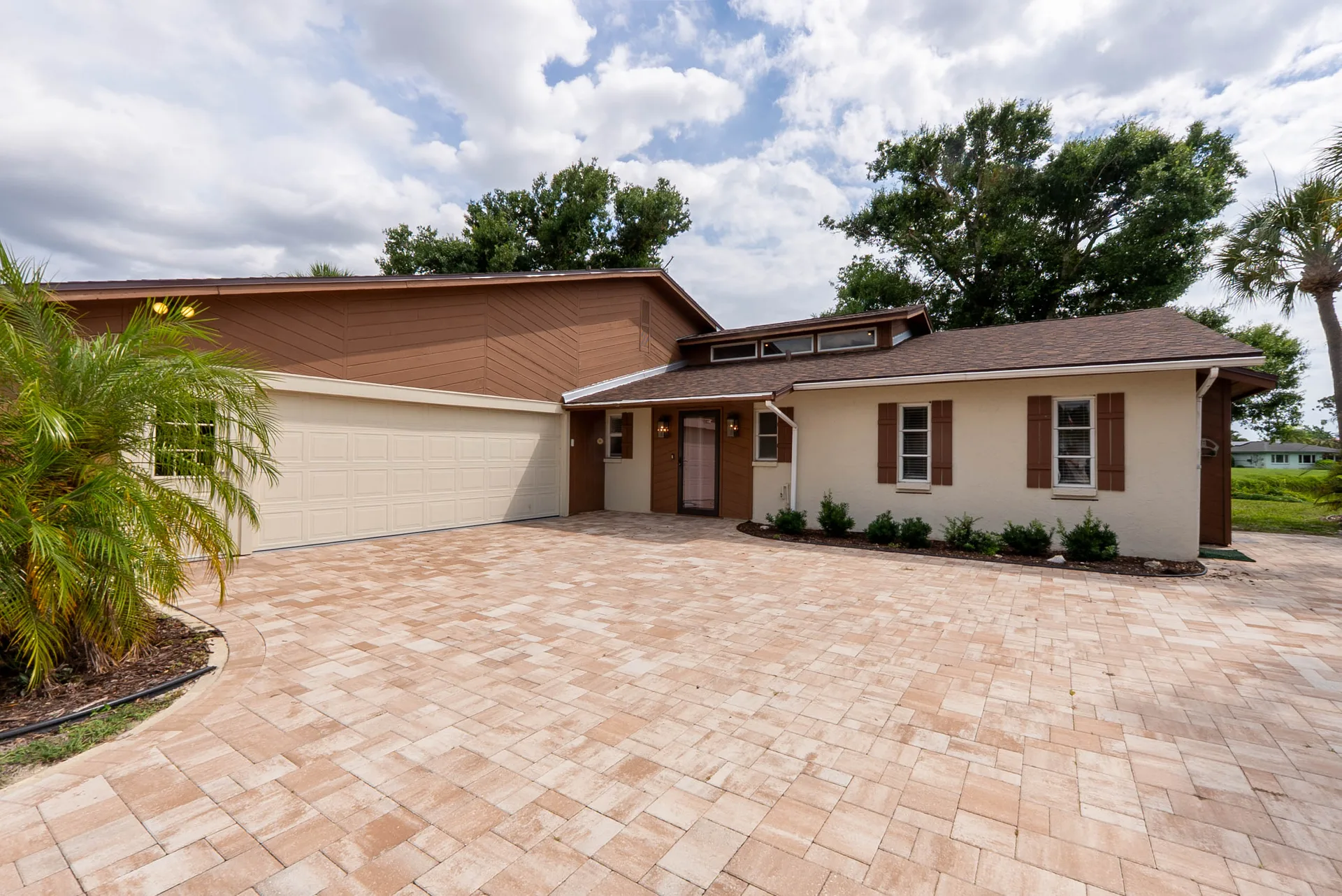 Front exterior of 1141 Sleepy Hollow Court in Venice, Florida, with a paver driveway, mature oak trees, tropical landscaping, and a two-car garage