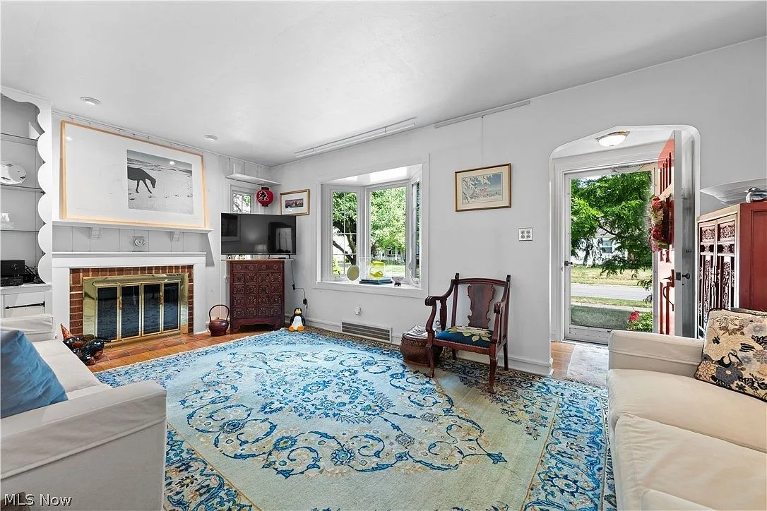 Living room with wood-burning fireplace, hardwood floors, and bay window