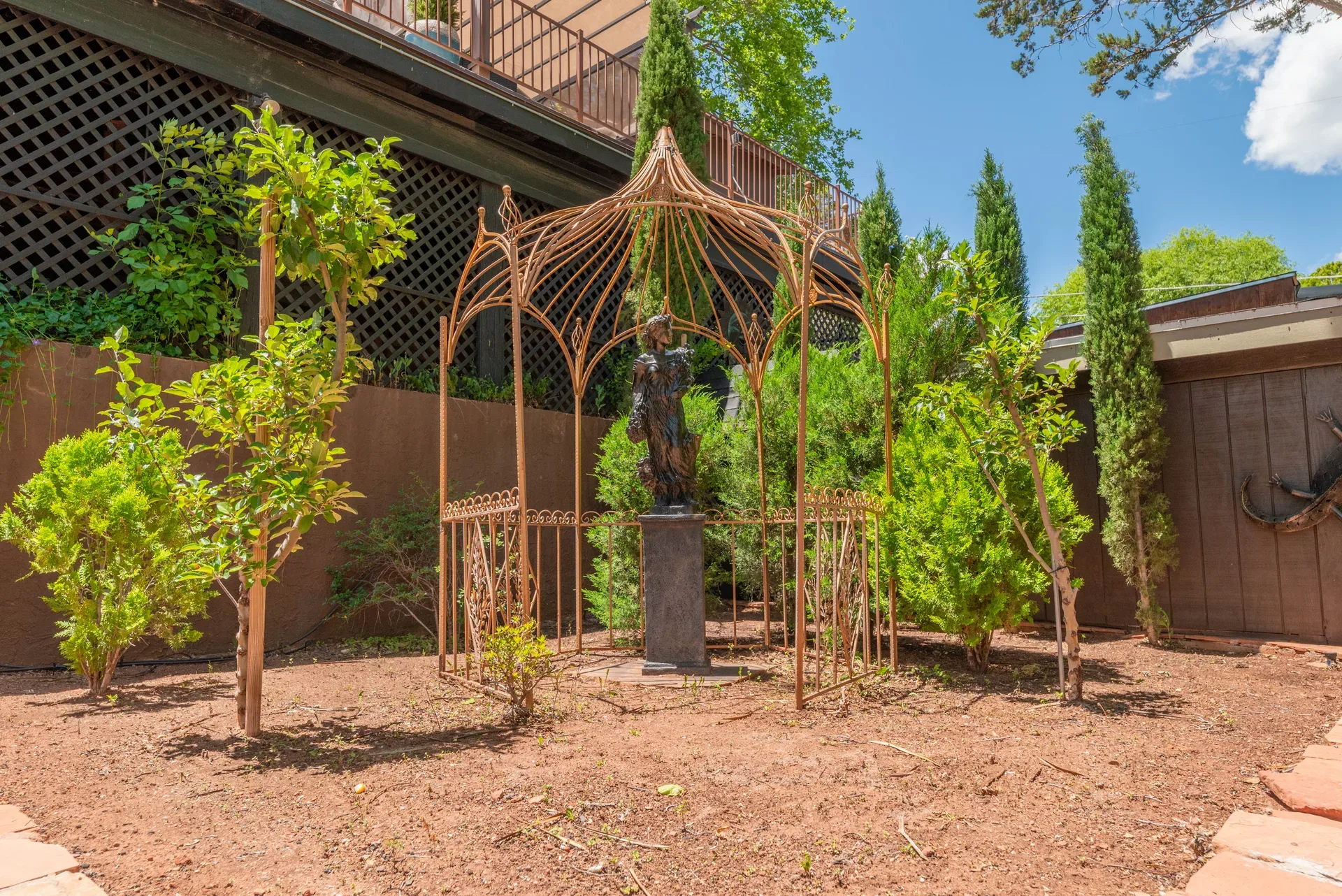 Decorative metal gazebo with bronze statue in garden setting