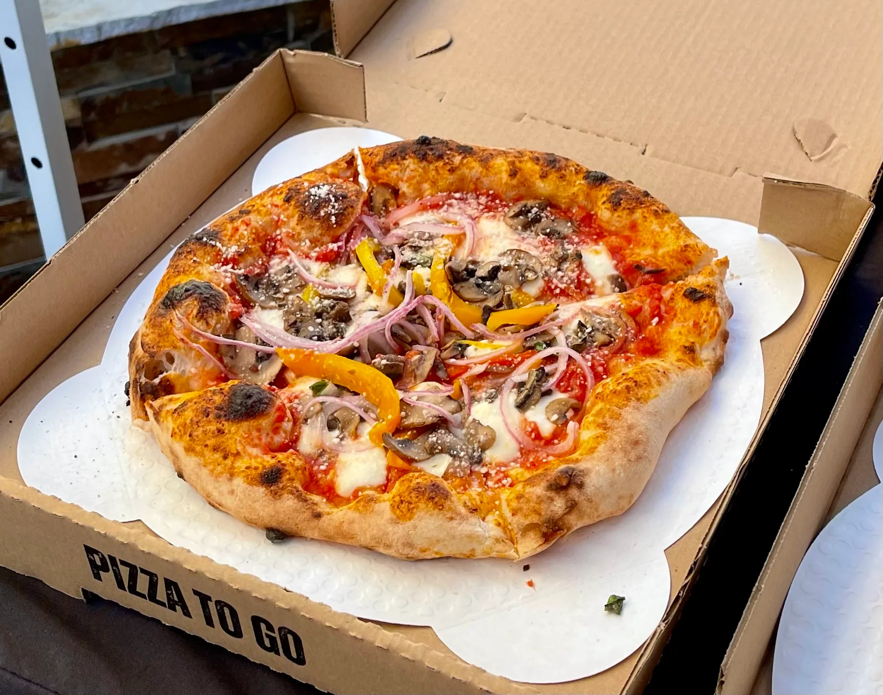 Fresh gourmet pizza with mushrooms, red onion, and bell pepper in a takeout box ready for pickup