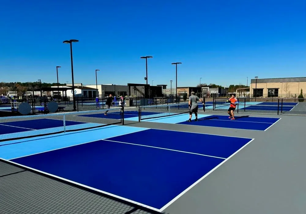 Players on outdoor pickleball courts with blue and green surfaces, white lines, and chain-link fencing on a sunny day