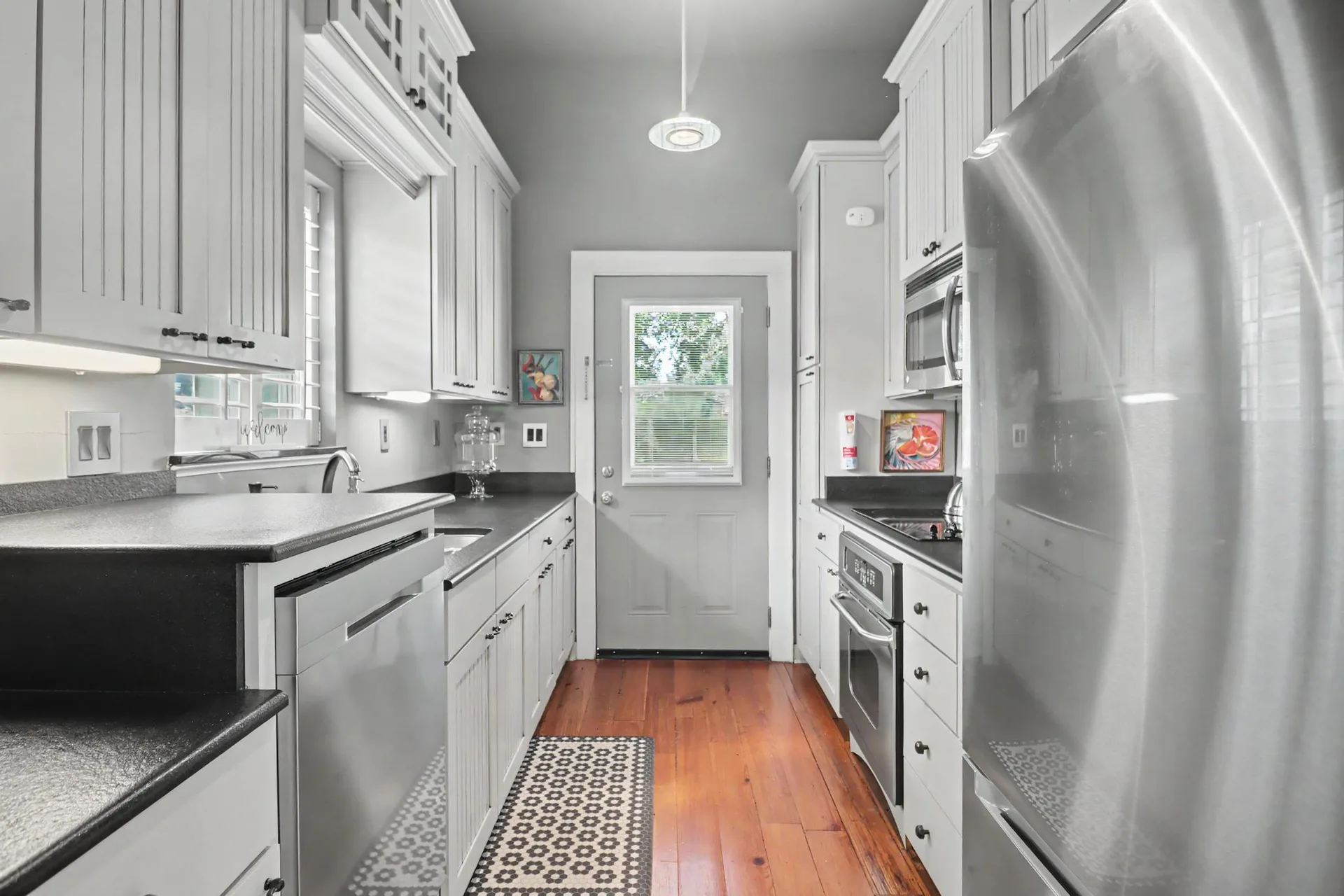 Galley-style kitchen with white cabinetry, black countertops, and heart pine flooring