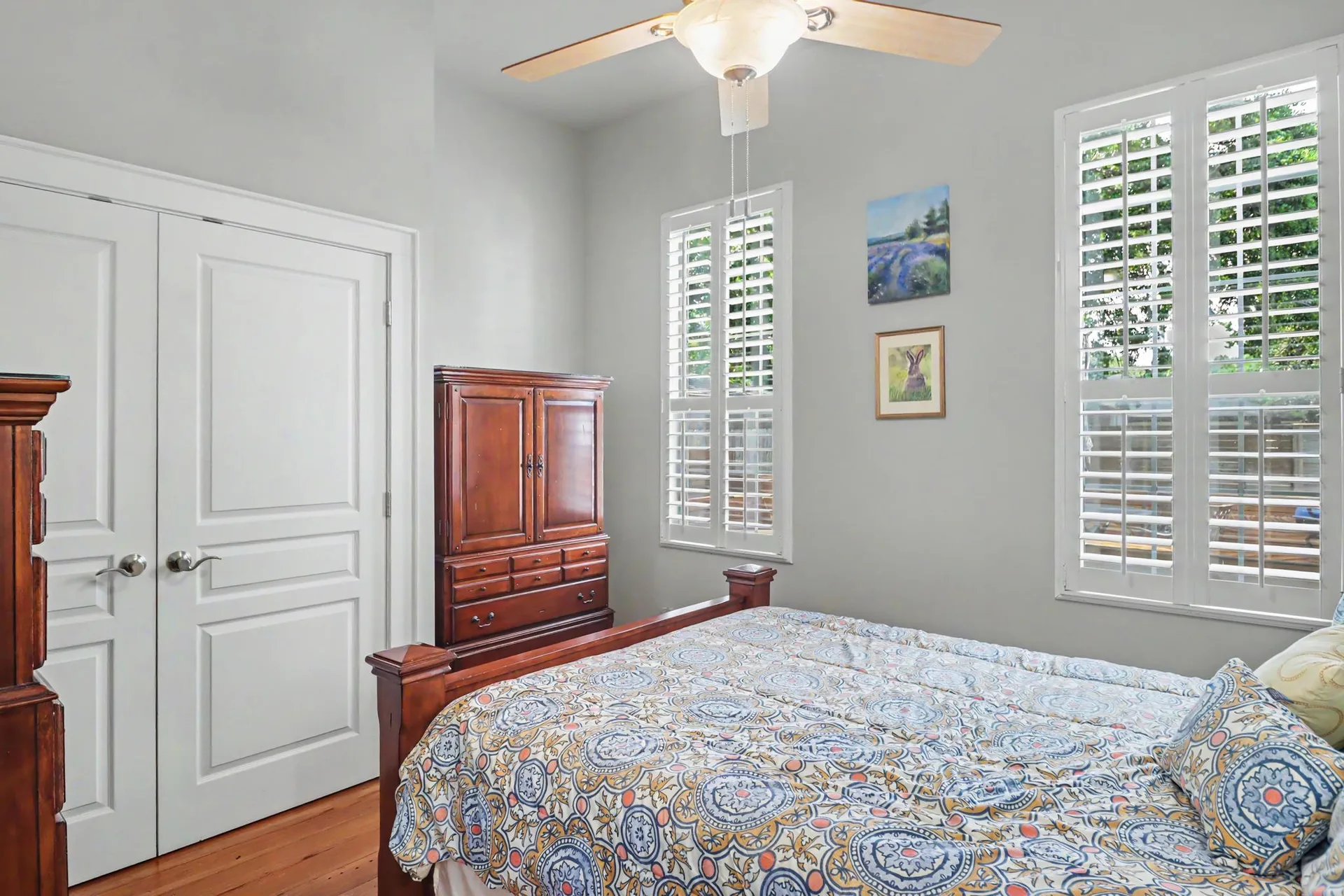 Primary bedroom with light gray walls, heart pine floors, and plantation shutters