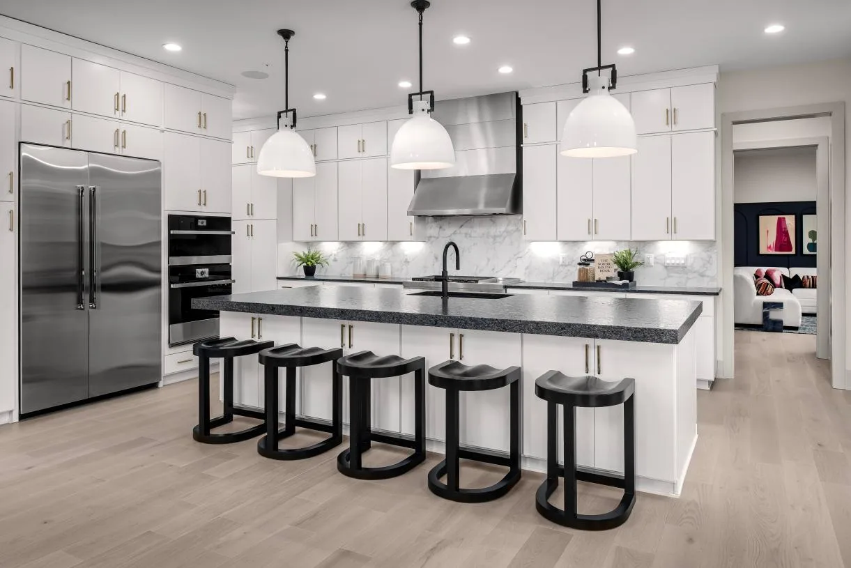 Modern bright kitchen with white cabinetry, dark stone island, stainless steel appliances, and light wood flooring