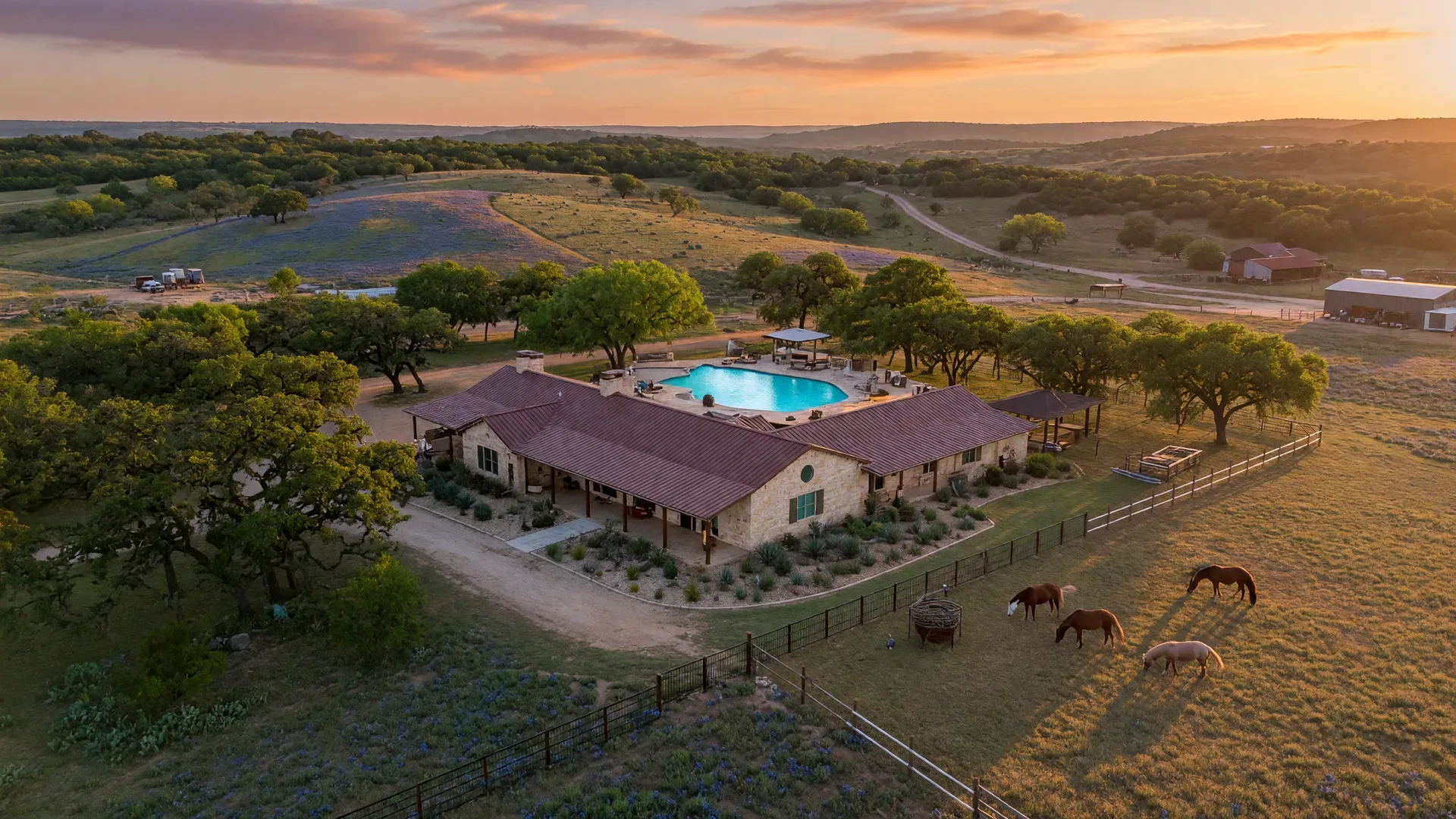 Aerial view of a Texas Hill Country ranch estate with pool and horse pasture at sunset