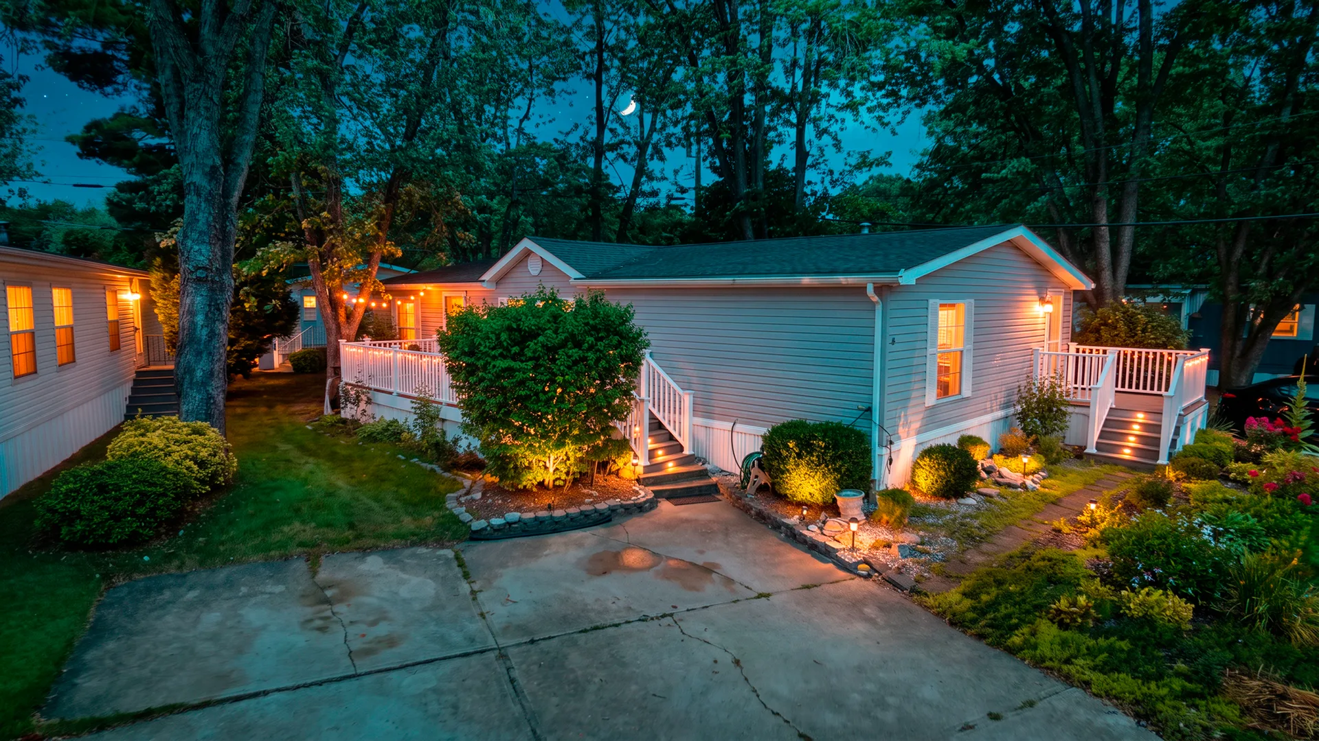 Dusk aerial view of the manufactured home at 2528 Tilton Rd. Lot #48, with deck string lights and landscape lighting
