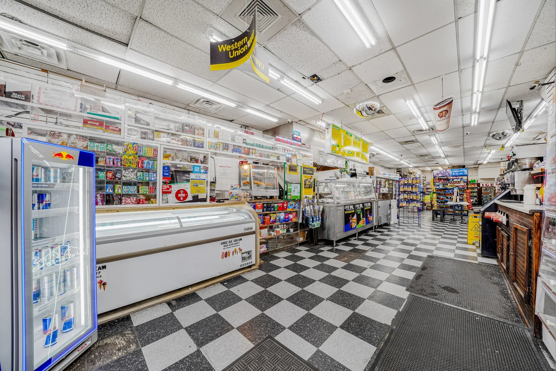 Supermarket interior showing beverage coolers, chest freezers, retail shelving, and service counter