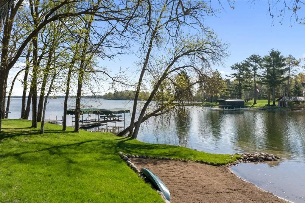 Backyard lakefront view with green grass, trees, and boat dock with canopy