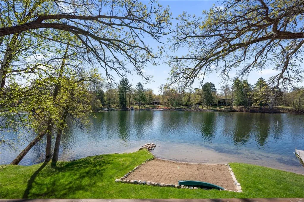 Backyard shoreline view with grass lawn, sandy patch, and mature deciduous trees