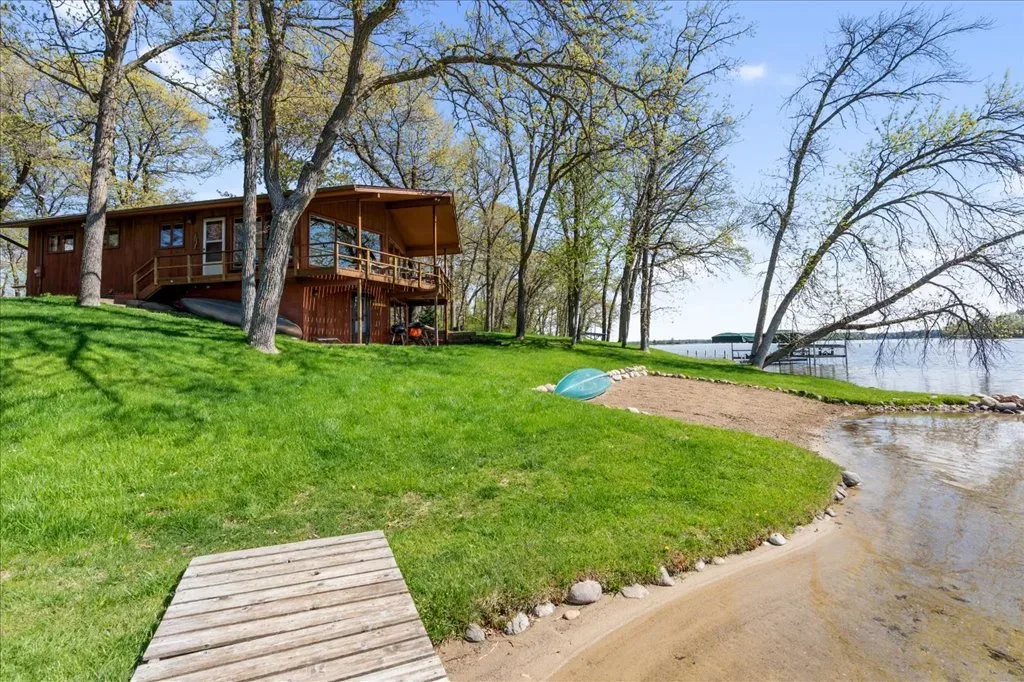 Backyard and lakeshore view with lawn, sandy area, dock, and water