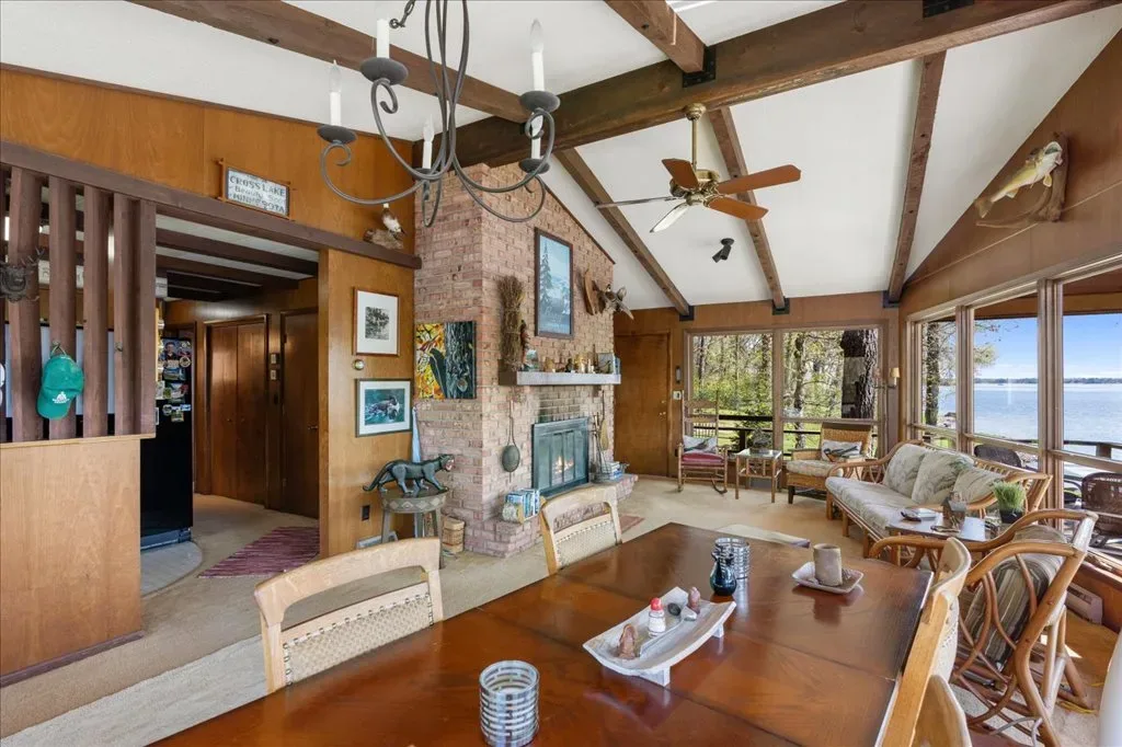 Rustic living and dining area with wood-paneled walls, exposed beams, and brick fireplace