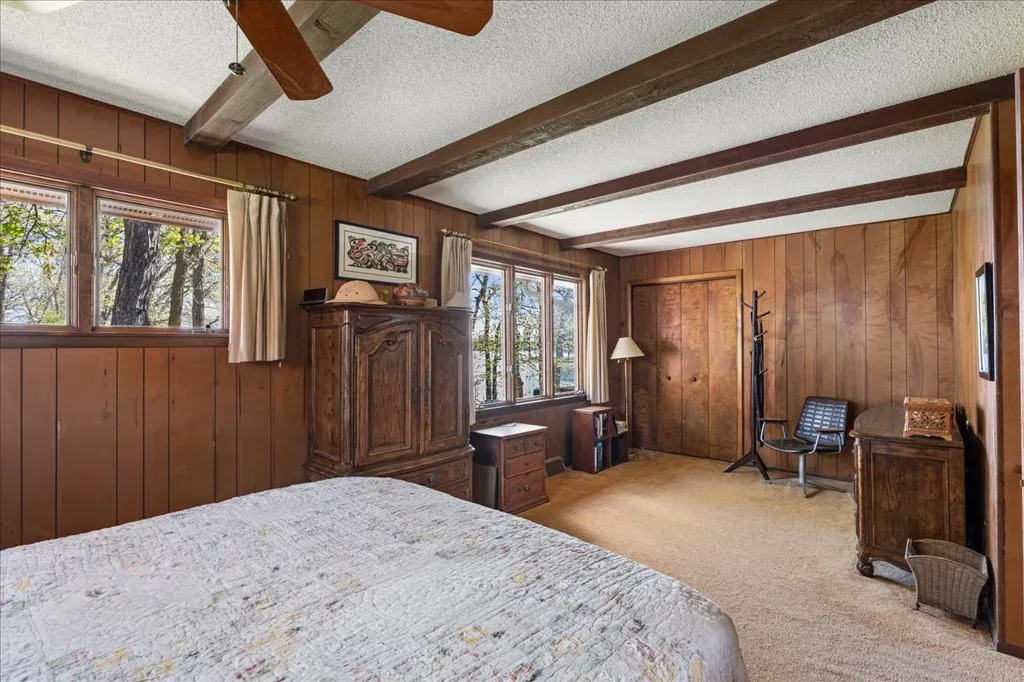 Master bedroom with wood-paneled walls and exposed ceiling beams