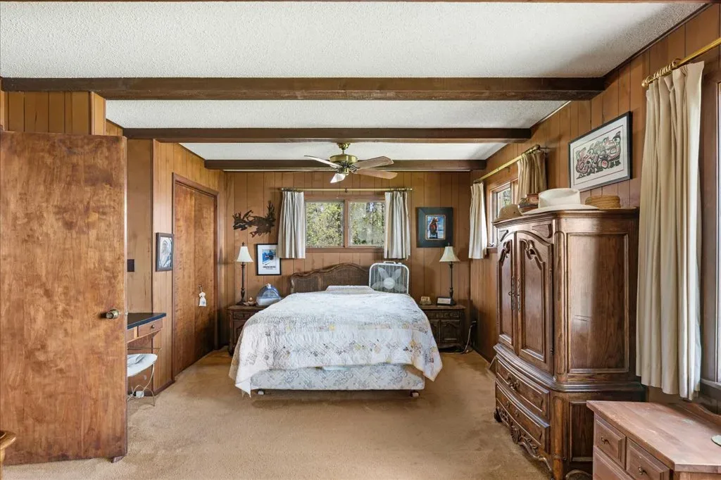 Bedroom with wood-paneled walls, exposed ceiling beams, and beige carpeting