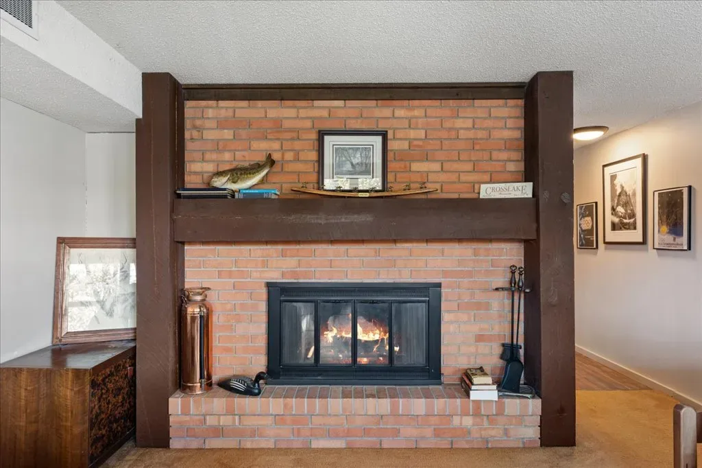 Living room focused on red brick fireplace with dark wood mantle and structural pillars