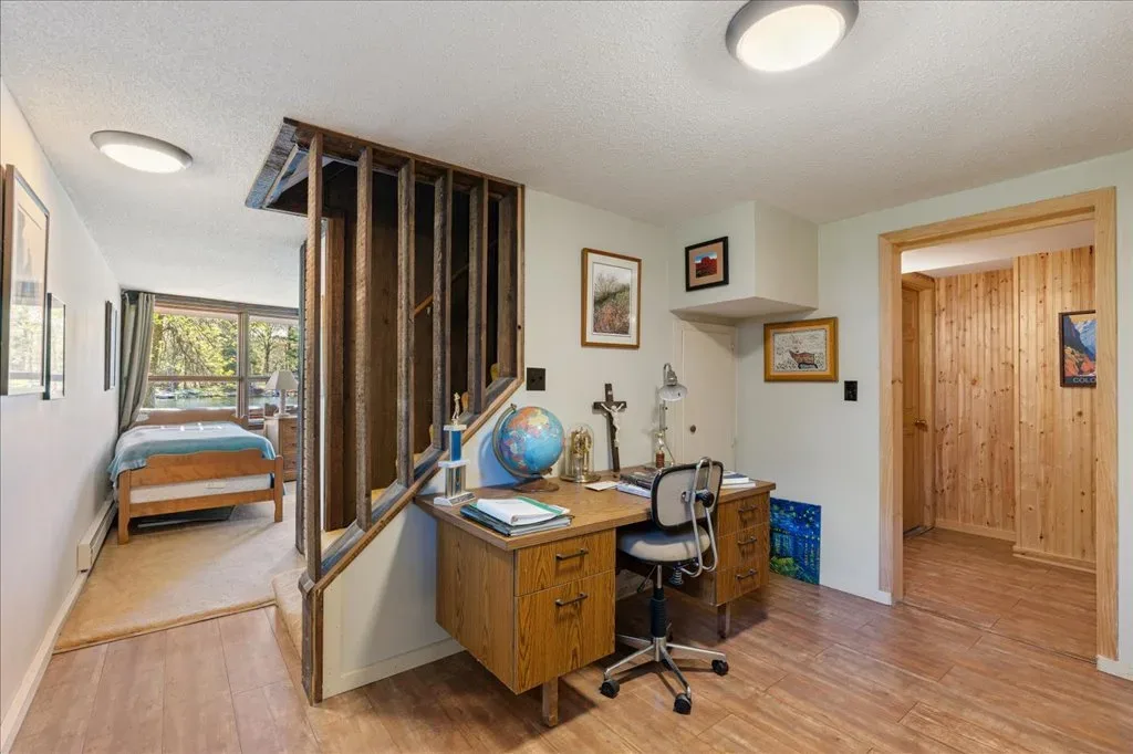 Bedroom with adjoining home office area, wood-look flooring, and rustic staircase railing