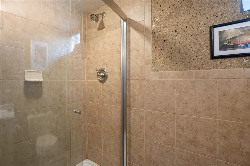 Walk-in shower with tan ceramic tiles, pebble stone accent, and chrome hardware