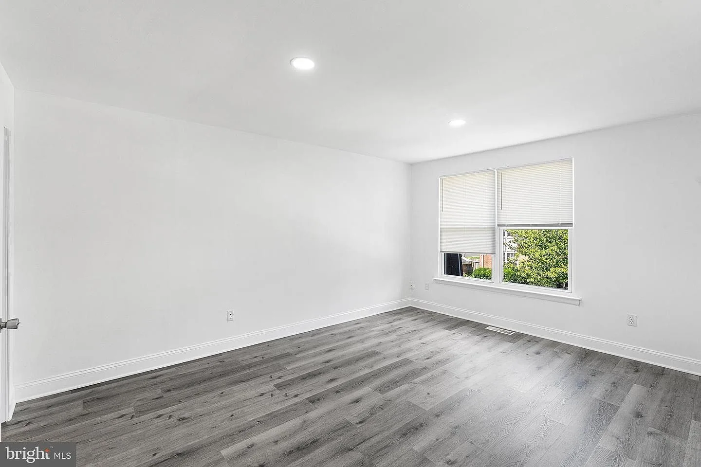 Bright secondary bedroom with natural daylight and gray wood-look flooring
