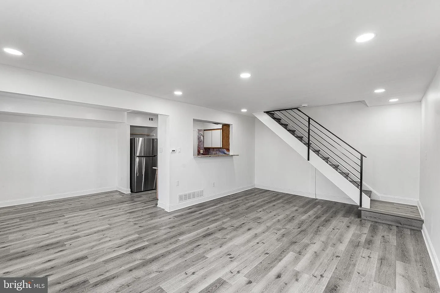 Spacious living room with gray wood-look laminate flooring and staircase with black metal railing