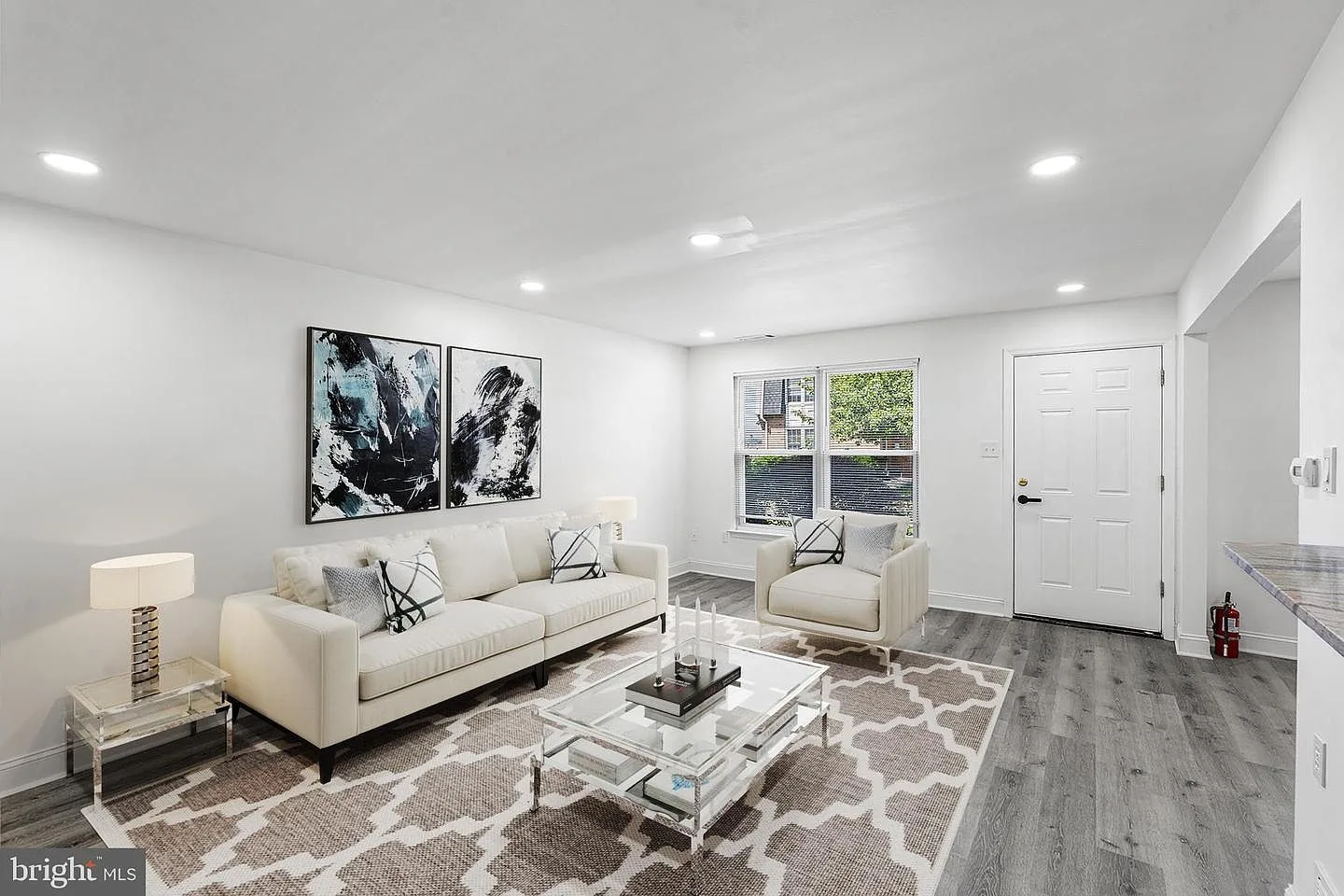 Modern living room with staged furniture, abstract art, and gray wood-look flooring