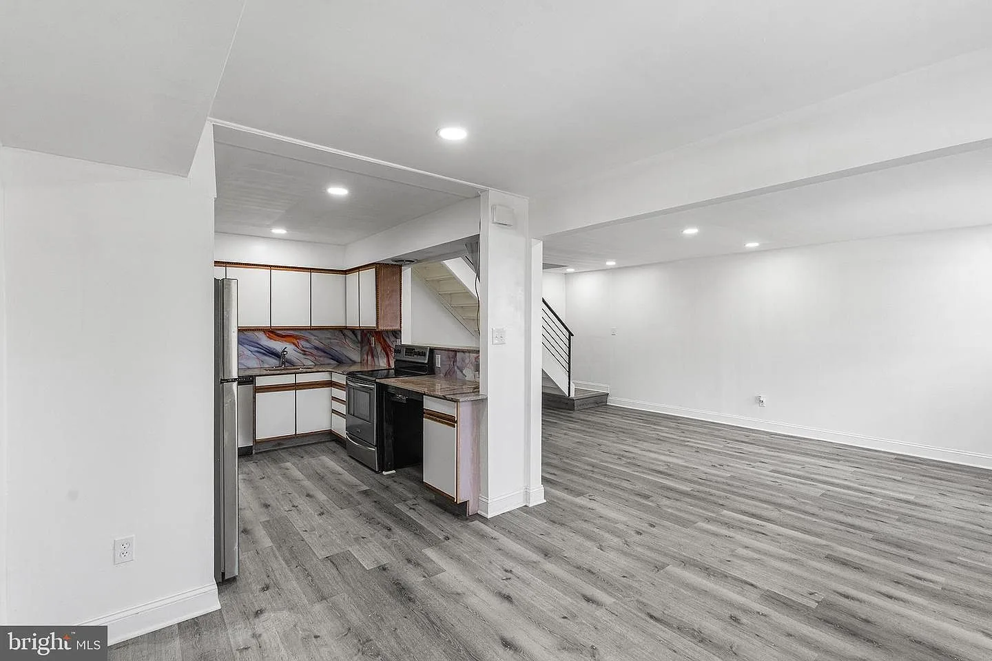 Open plan kitchen connected to empty living area with gray flooring