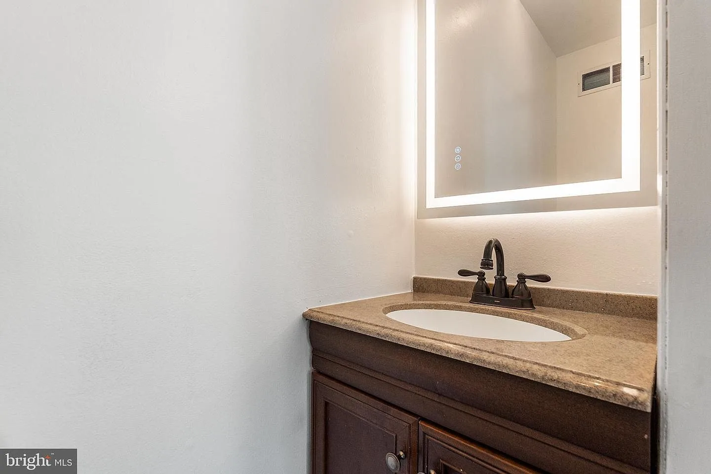 Modern bathroom vanity with dark wood cabinet, LED-backlit mirror, and oil-rubbed bronze faucet