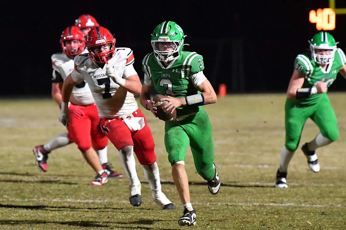High school football game under stadium lights with players in red and green uniforms on the field in Cary, NC