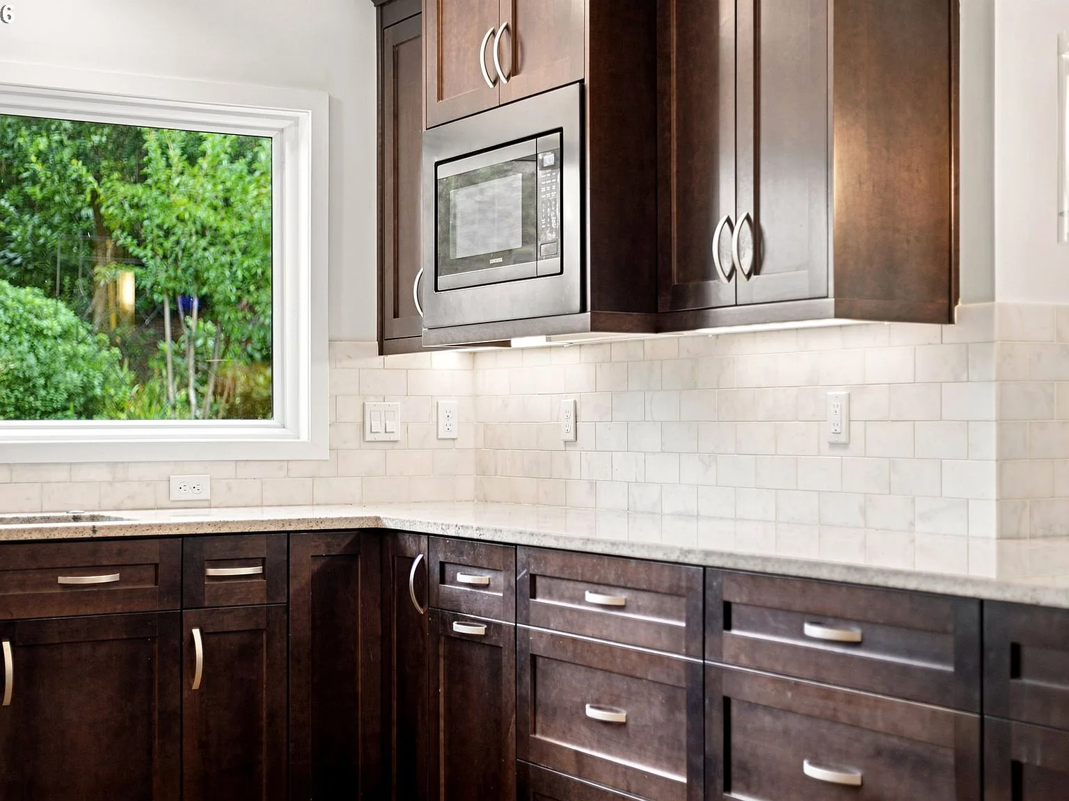 Kitchen close-up showing dark stained shaker cabinetry and marble-look tile backsplash