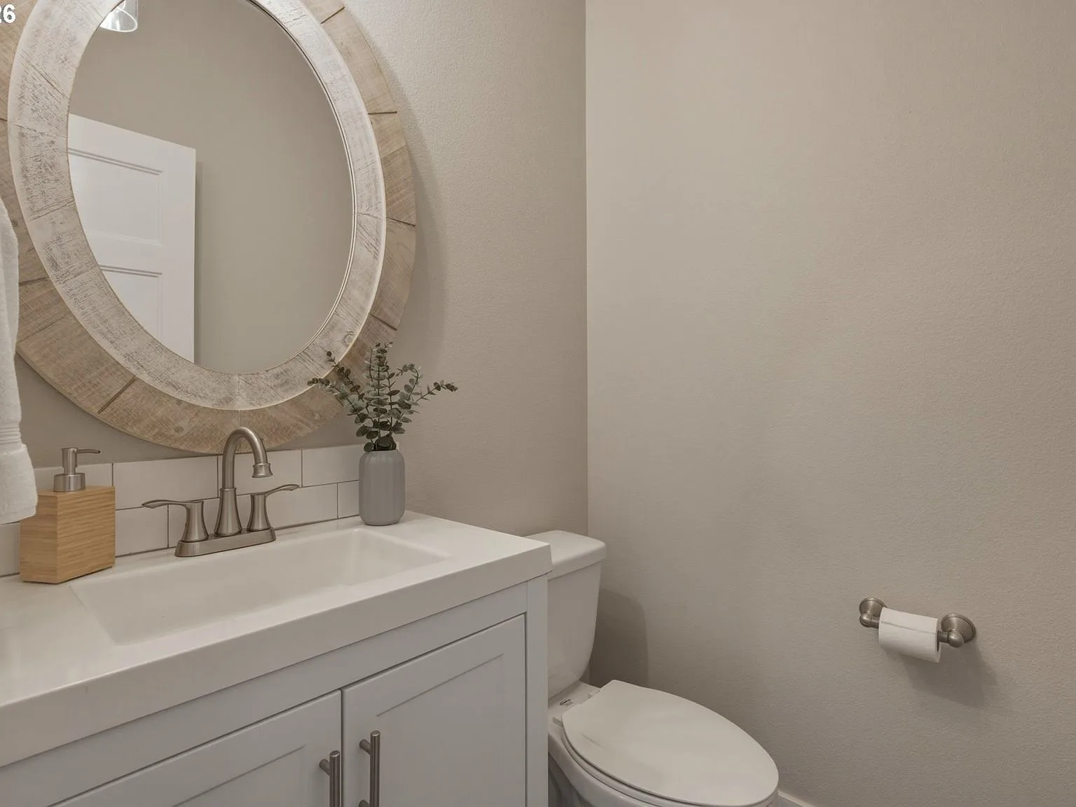 Powder room with white vanity, subway tile, and circular wood-framed mirror