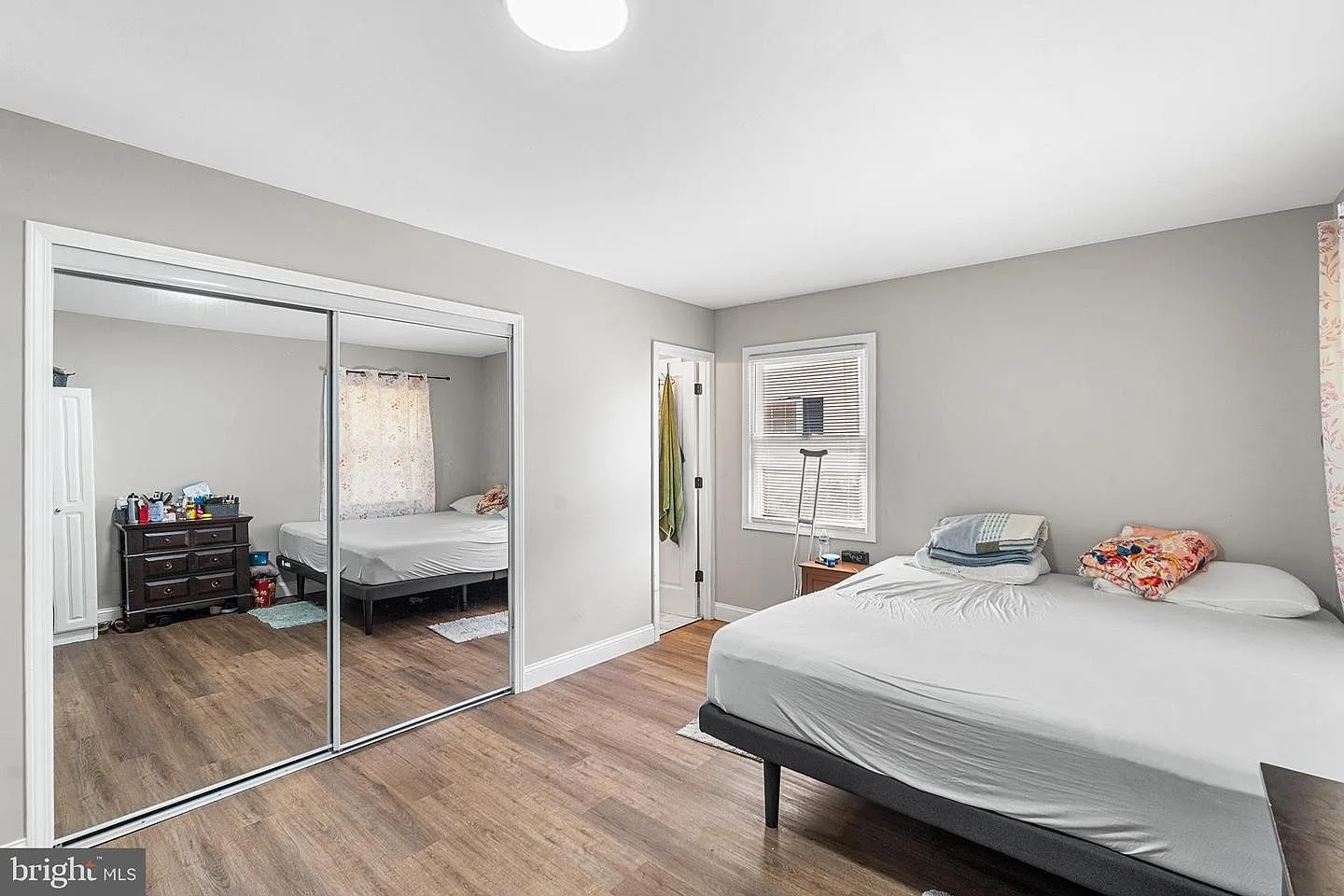 Bedroom with neutral grey walls, wood-look plank flooring, and mirrored closet doors