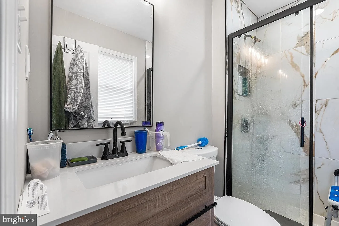 Modern renovated bathroom with wood-grain vanity, white quartz countertop, and marble-look wall tile