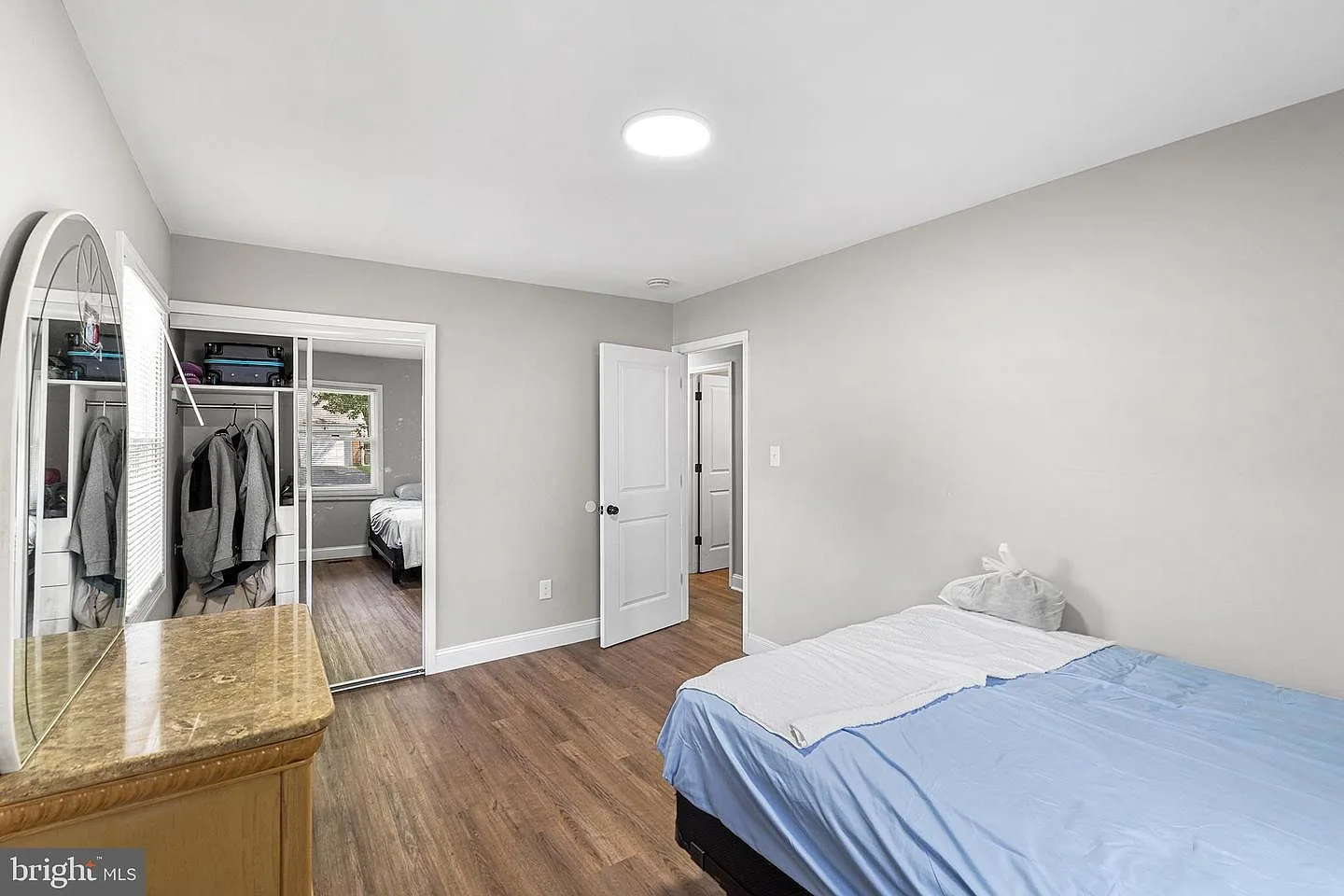 Bedroom with light gray walls, wood-look flooring, and vanity area