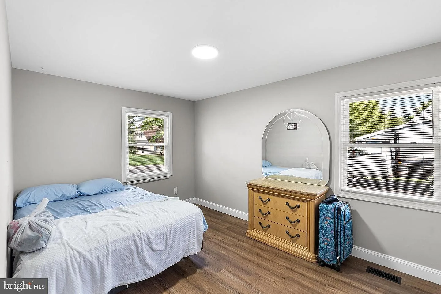 Renovated bedroom with light grey walls, two windows with natural daylight, and dark wood-look flooring