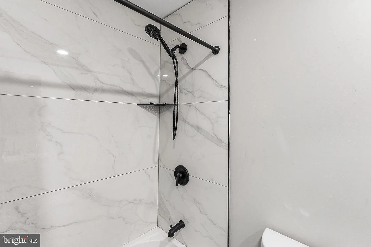 Modern bathroom shower with white marble-look tiles, grey veining, and matte black fixtures