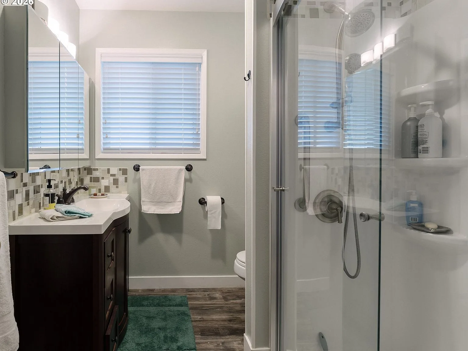 Updated hall bathroom with wood vanity, mosaic tile backsplash, and walk-in shower with glass doors