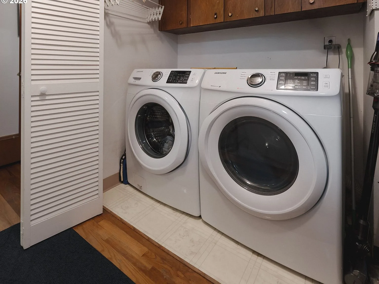 Laundry area with white front-load washer and dryer and upper cabinetry