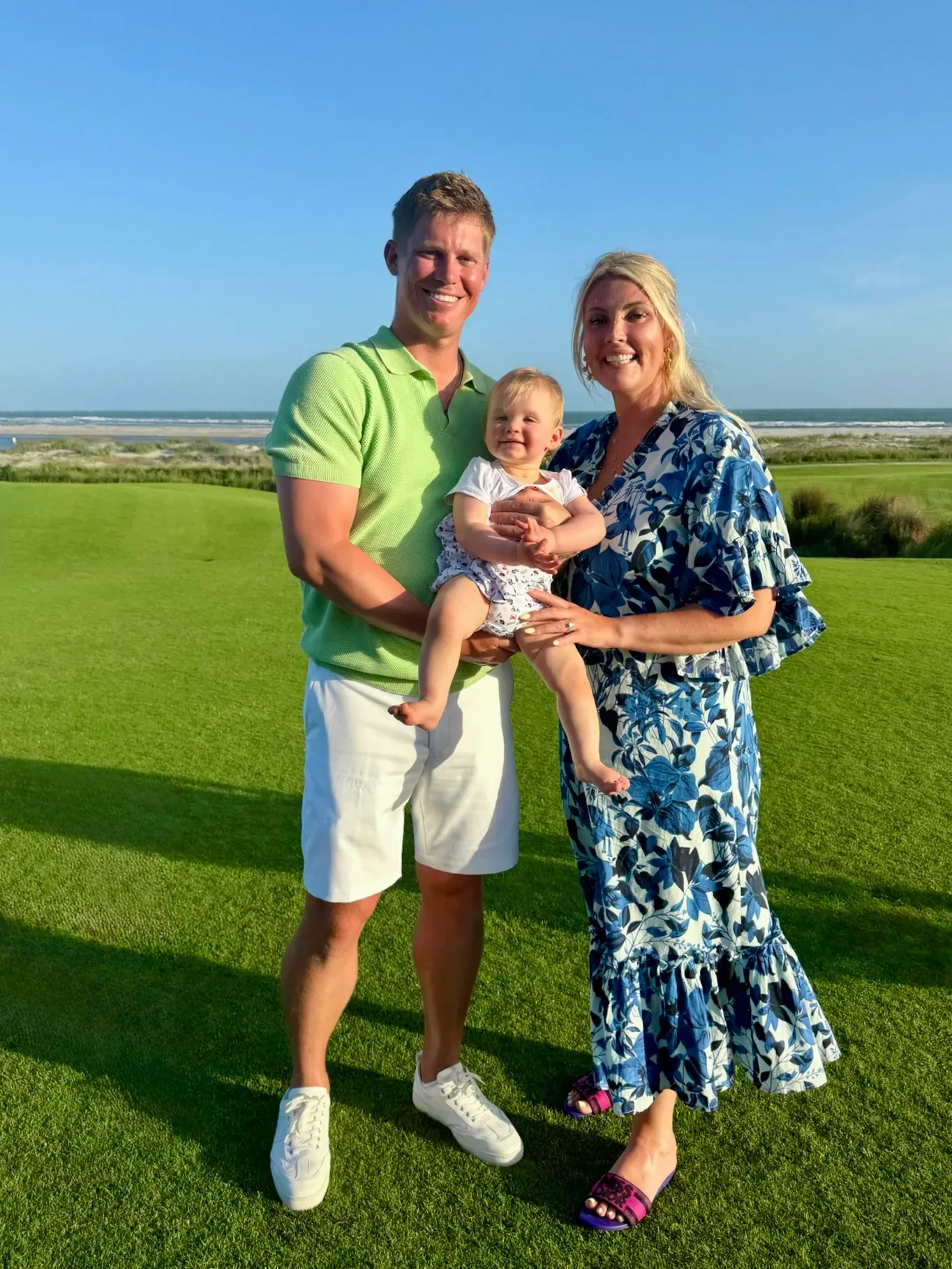 Austin Edwards with his wife and infant son standing on a coastal lawn with ocean views in the Florida Keys