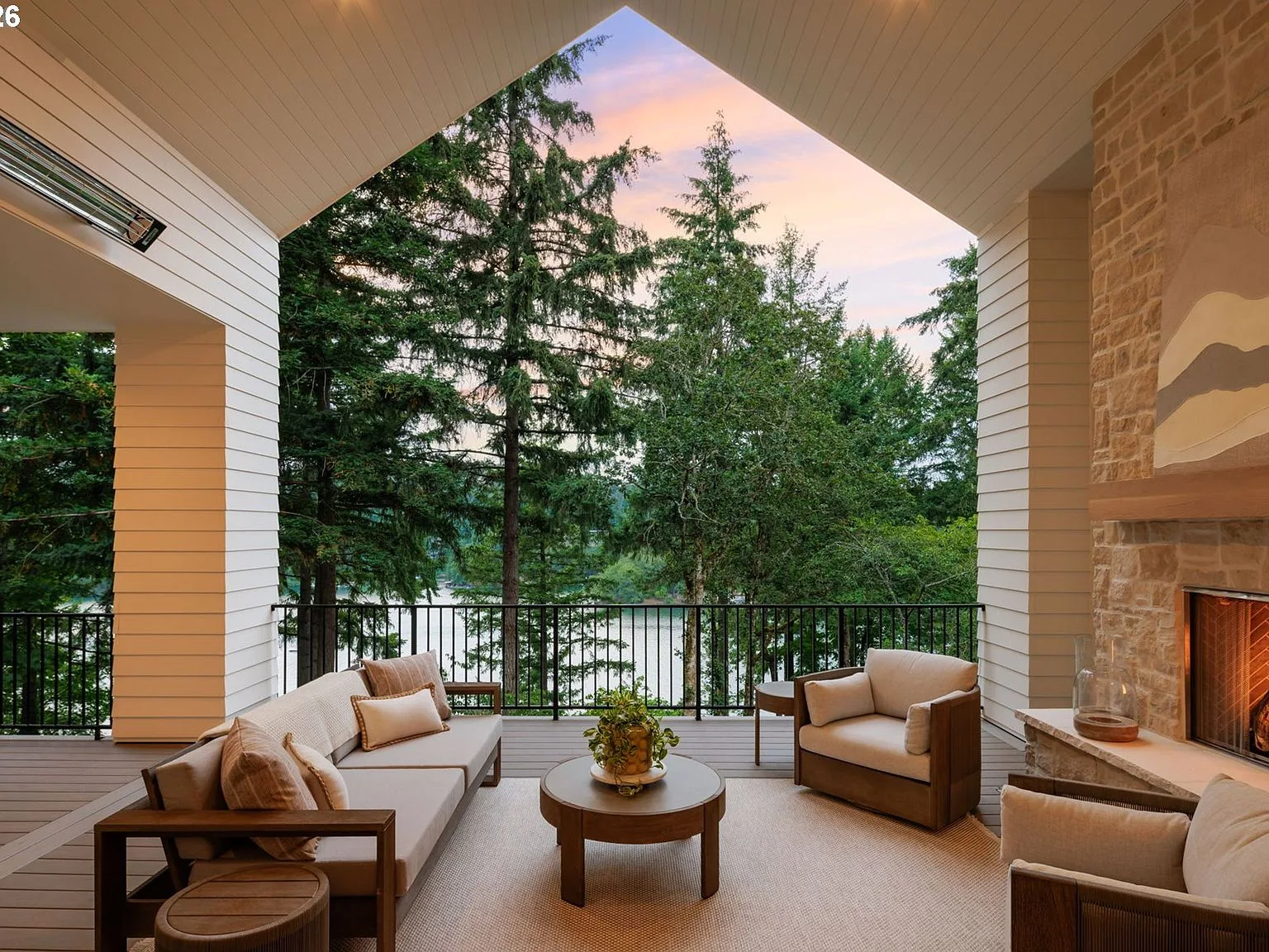 Covered terrace at dusk with stone fireplace, vaulted ceiling, and lake view