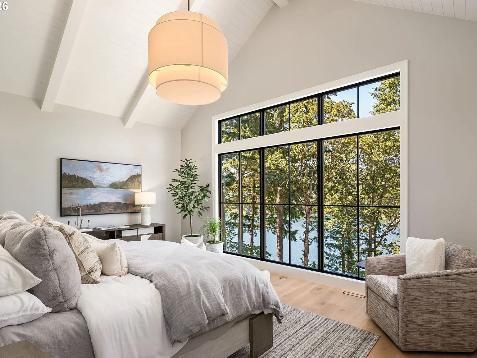 The primary bedroom with vaulted ceilings and lake views through black-framed windows